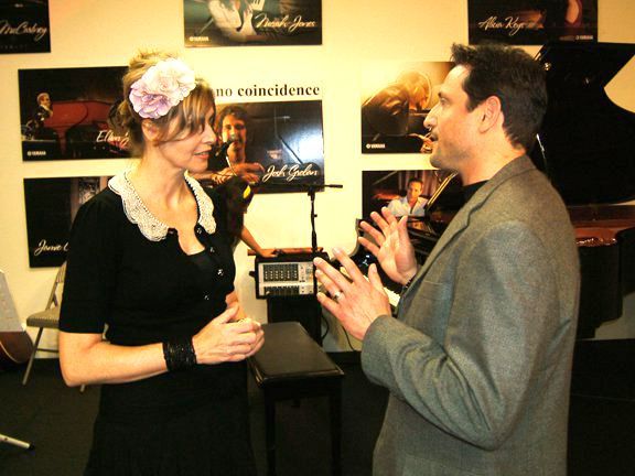 Fiona Joy Hawkins and Al in a gray suit talk in a music studio; posters of musicians on the wall.
