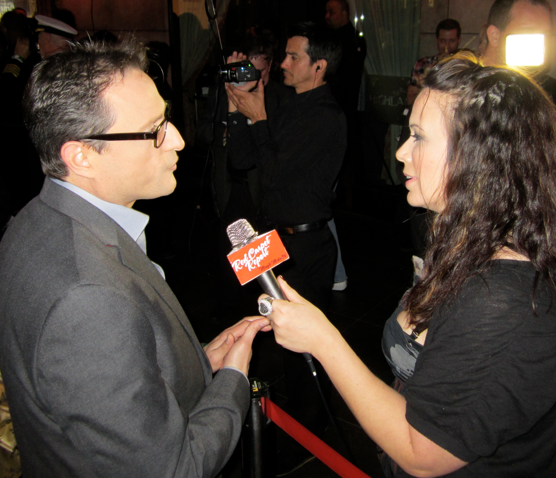 Al Conti being interviewed by woman at a red carpet event, cameras visible.