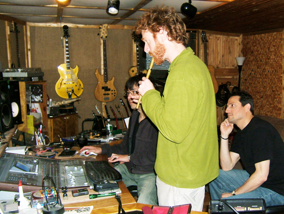 In recording studio, one plays a Celtic whistle. Guitars on the wall, mixing board in front.