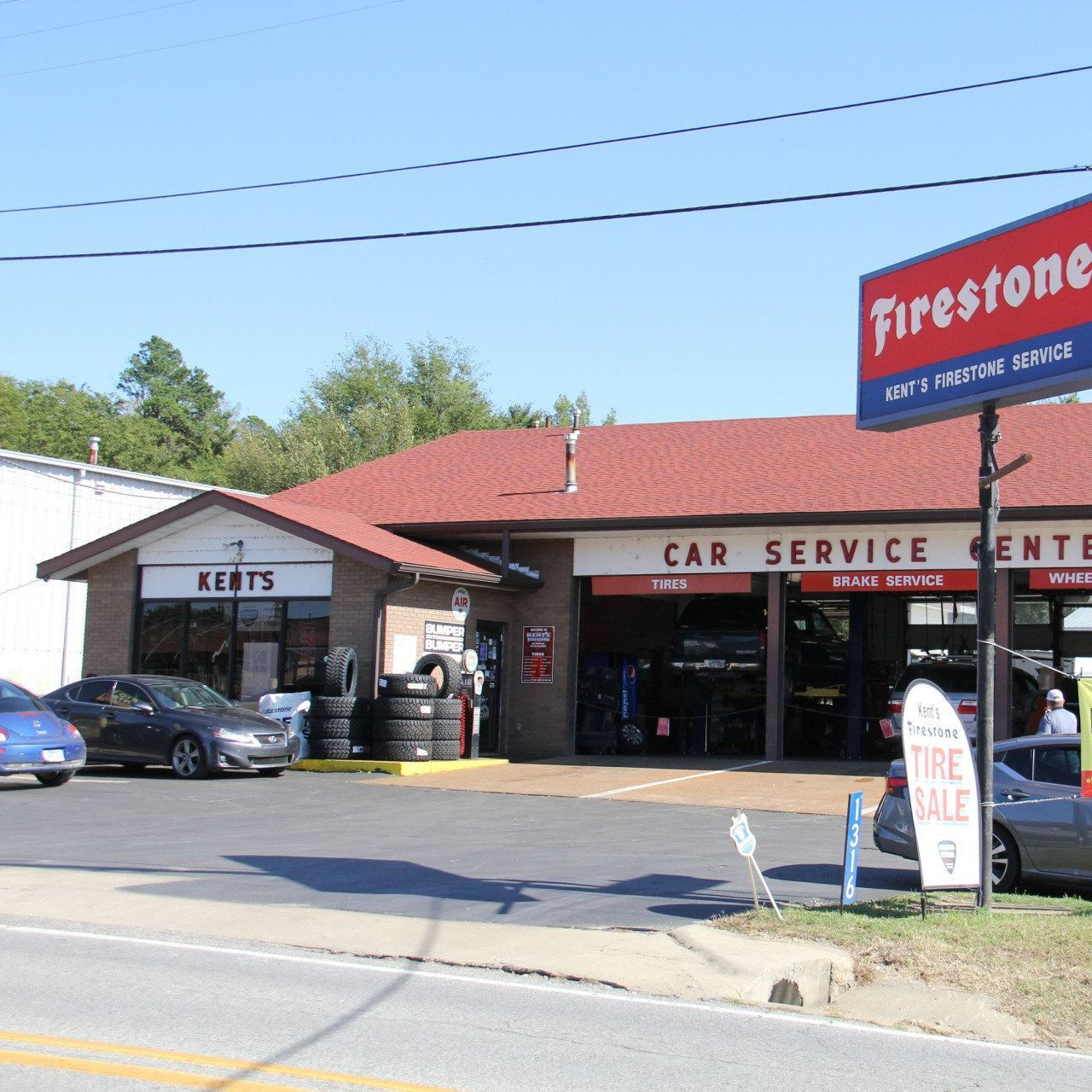 Firestone car service center with red roof, parked cars, and roadside sign on a sunny day