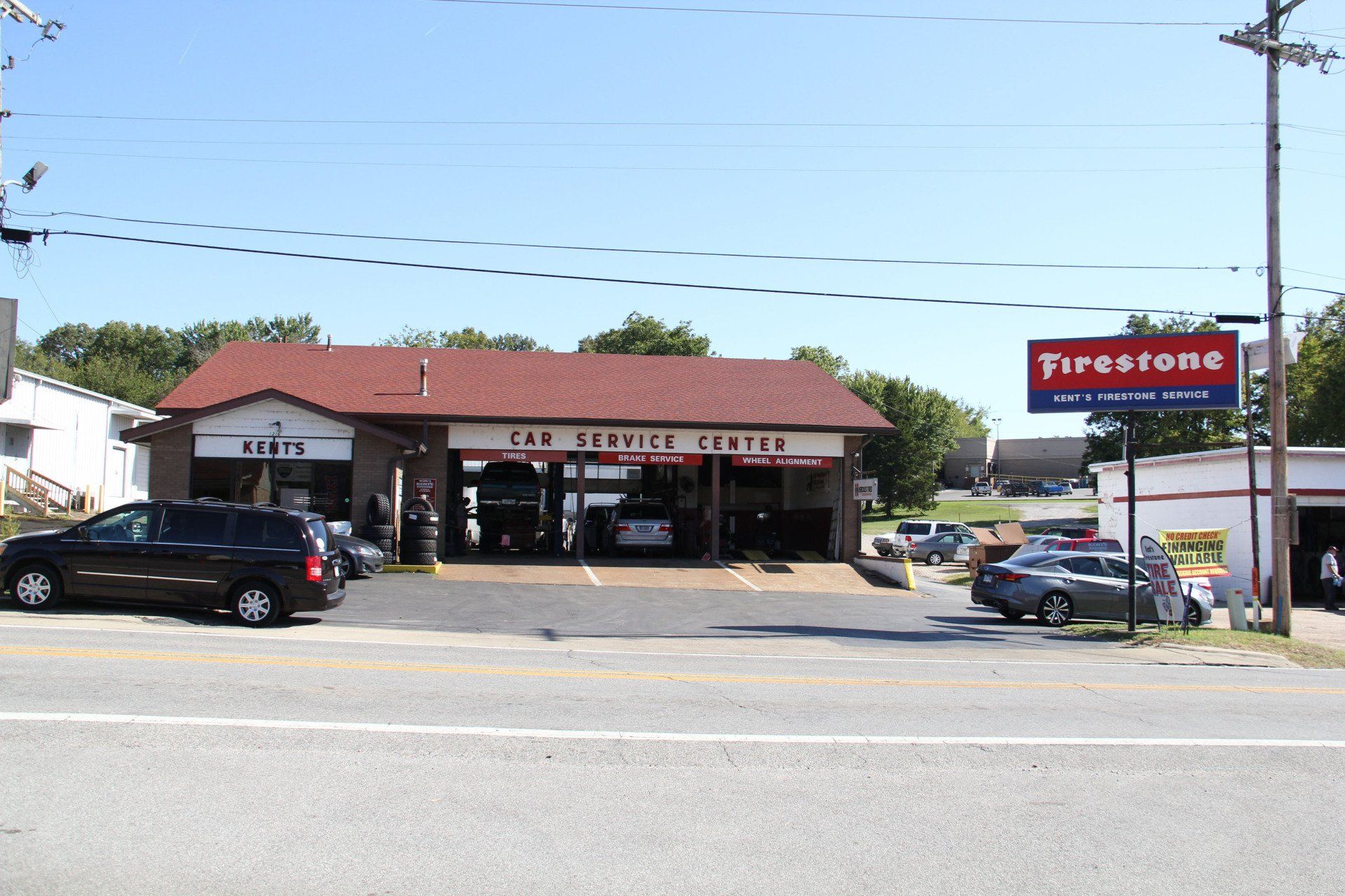 Auto repair shop with red roof and Firestone sign, cars parked outside along a roadside.