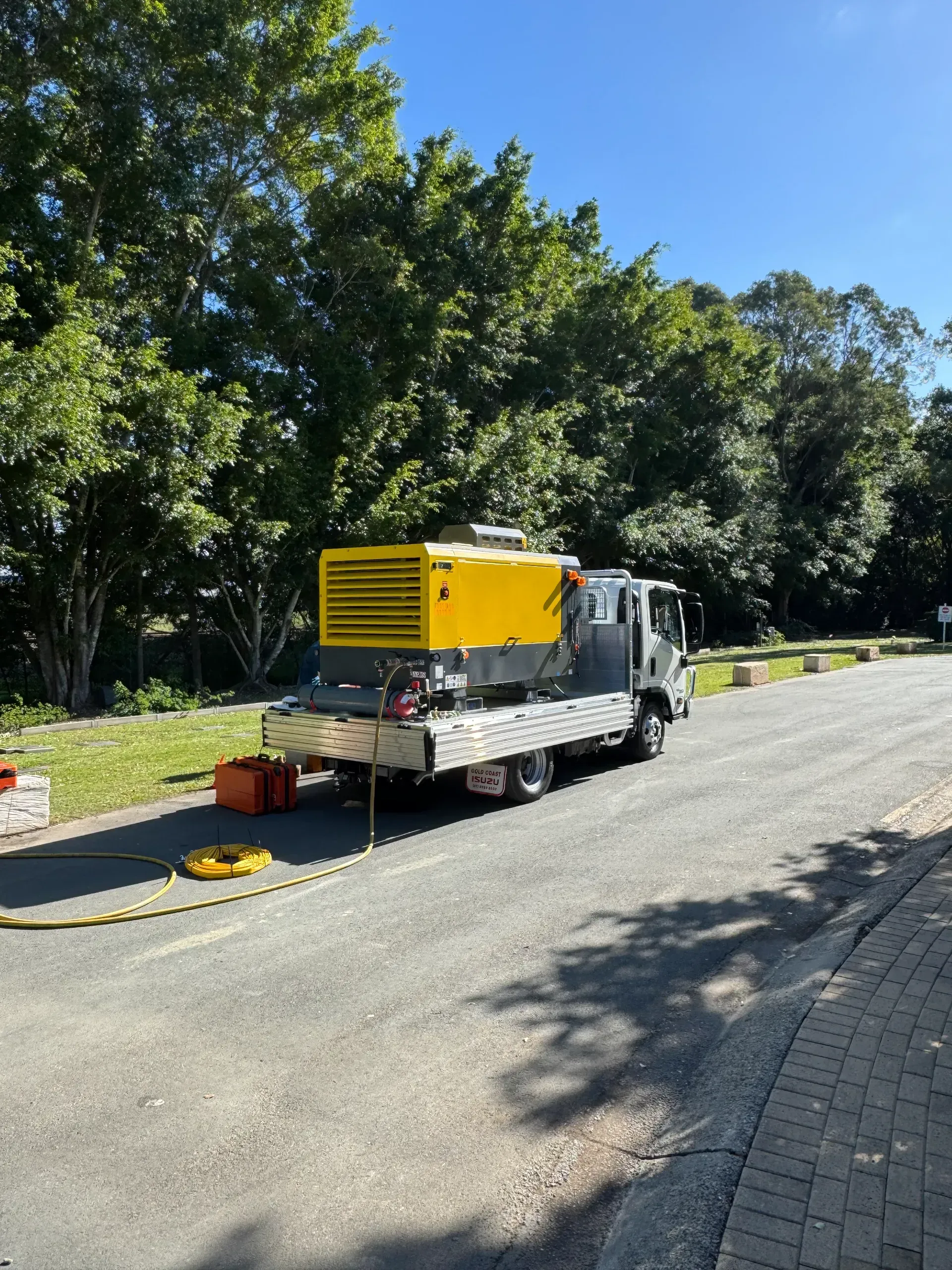 Yellow generator on a truck parked on a paved road, trees in the background.  — Commercial Leak Detection