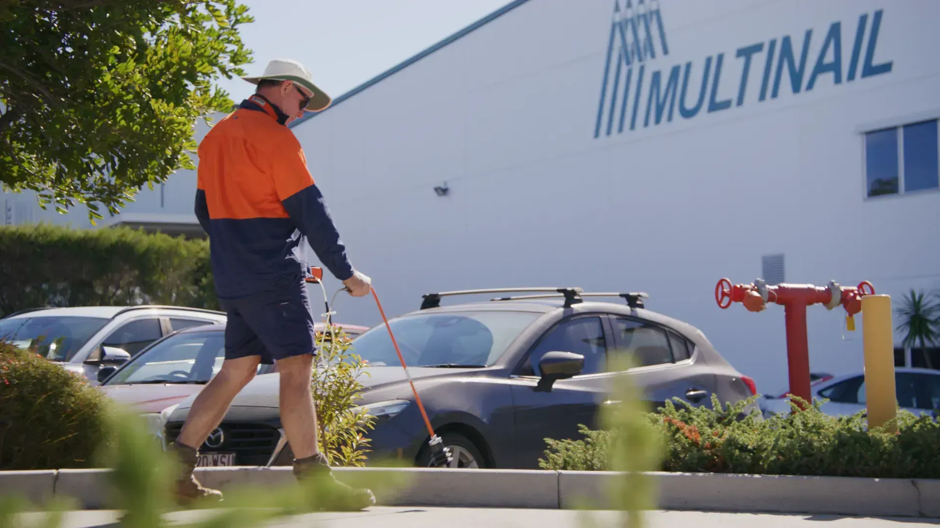 Worker In Orange Safety Vest Uses a Hose Outside the Multinail Building — Commercial Leak Detection in Mudgeeraba, QLD