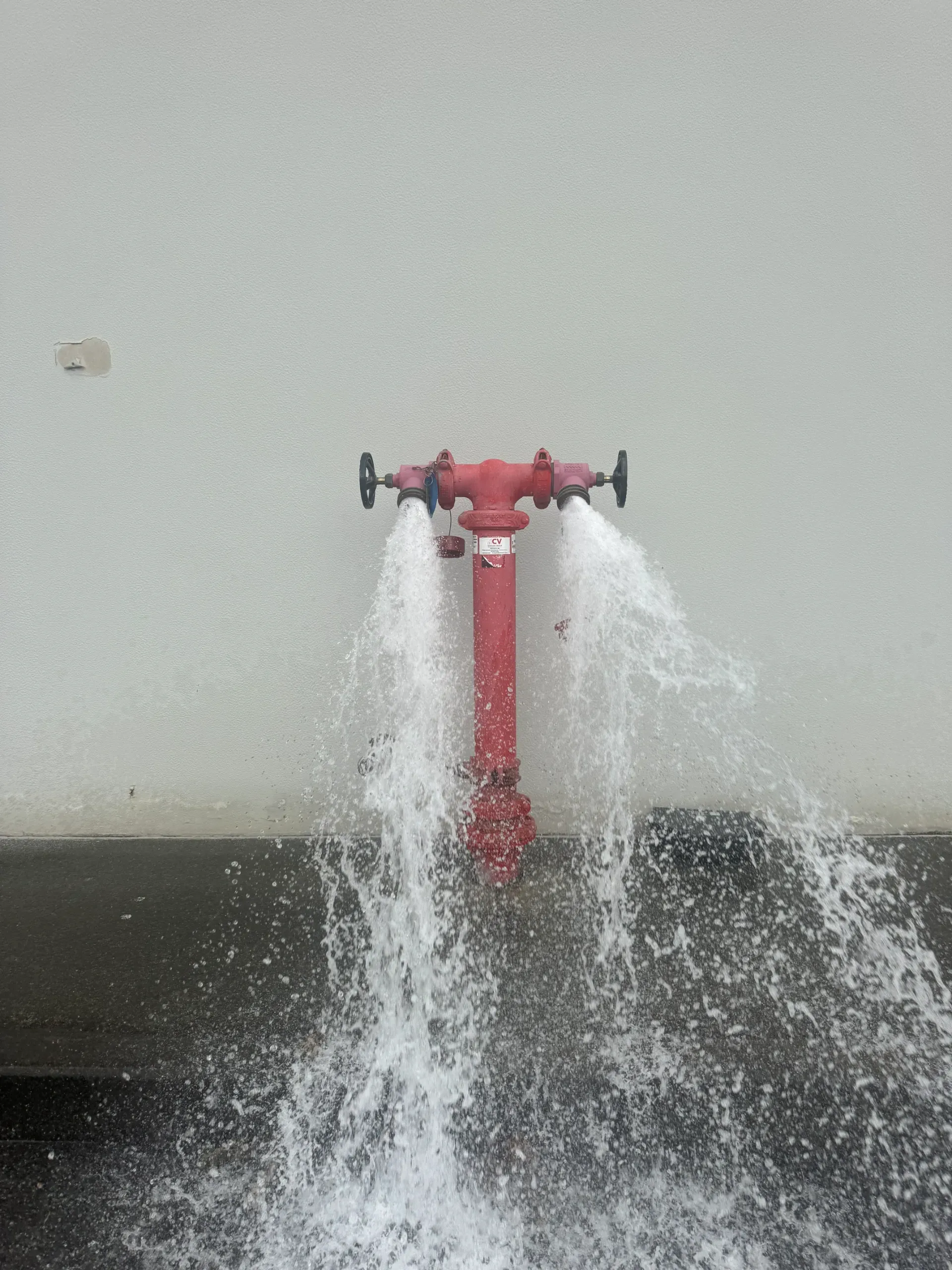 Red fire hydrant spurting water against a white wall.