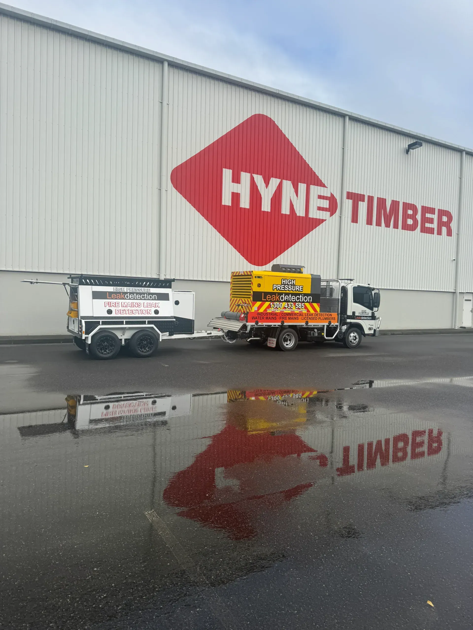 Truck and trailer in front of a Hyne Timber building with water reflection on wet pavement. — Commercial Leak Detection in South Brisbane, QLD