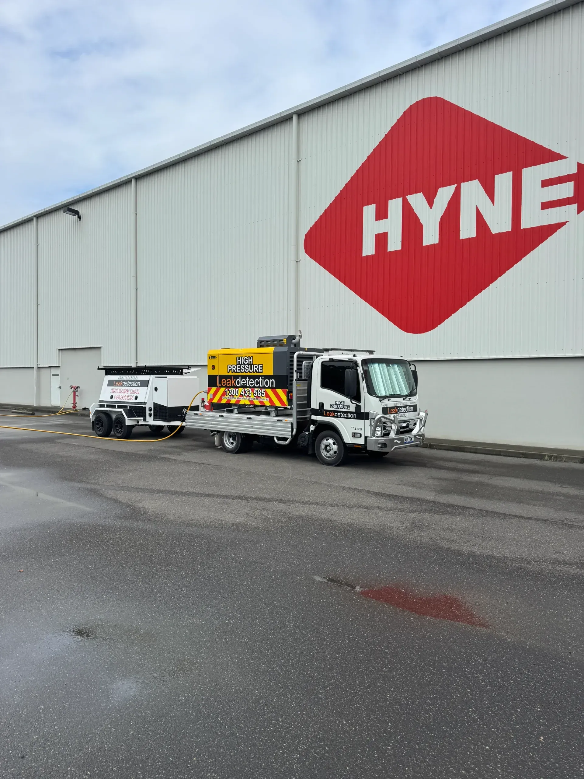 Truck with trailer parked in front of a Hyne building with a red and white logo. — Commercial Leak Detection