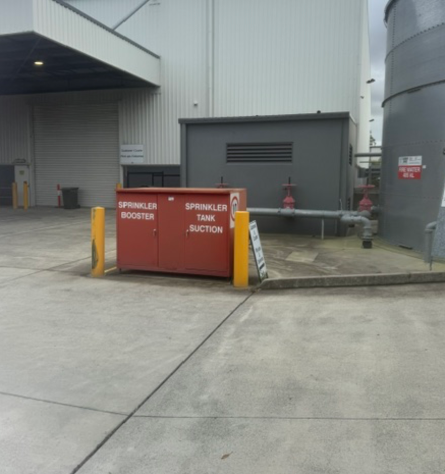 Sprinkler Booster Cabinet With Bollards Beside Warehouse And Water Tank &mdash; Commercial Leak Detection in Mudgeeraba, QLD