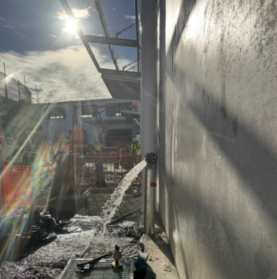 Water Discharging From Fire Main Valve Beside Concrete Wall — Commercial Leak Detection in Mudgeeraba, QLD