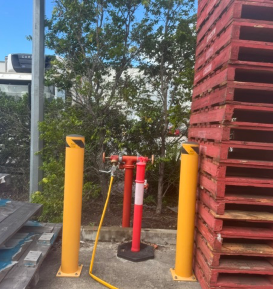 Fire Hydrant With Yellow Hose Between Bollards Beside Pallets &mdash; Commercial Leak Detection in Mudgeeraba, QLD