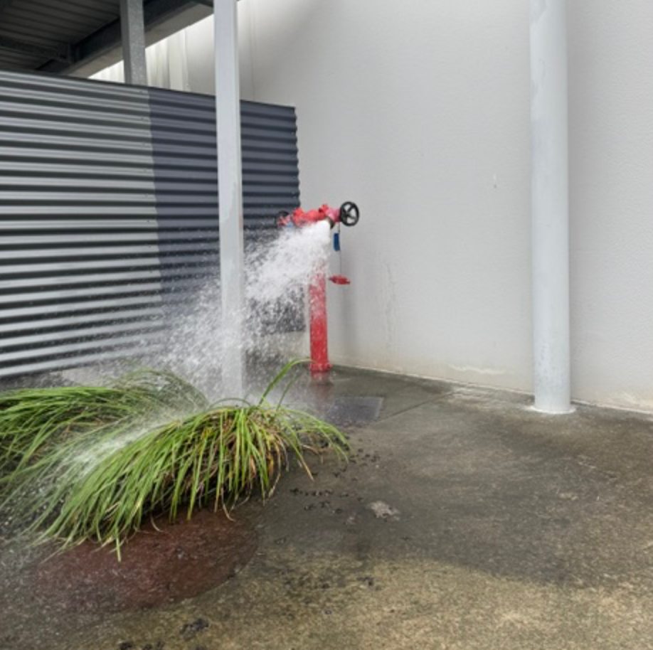 Red Fire Hydrant Spraying Water Beside Warehouse Wall &mdash; Commercial Leak Detection in Mudgeeraba, QLD