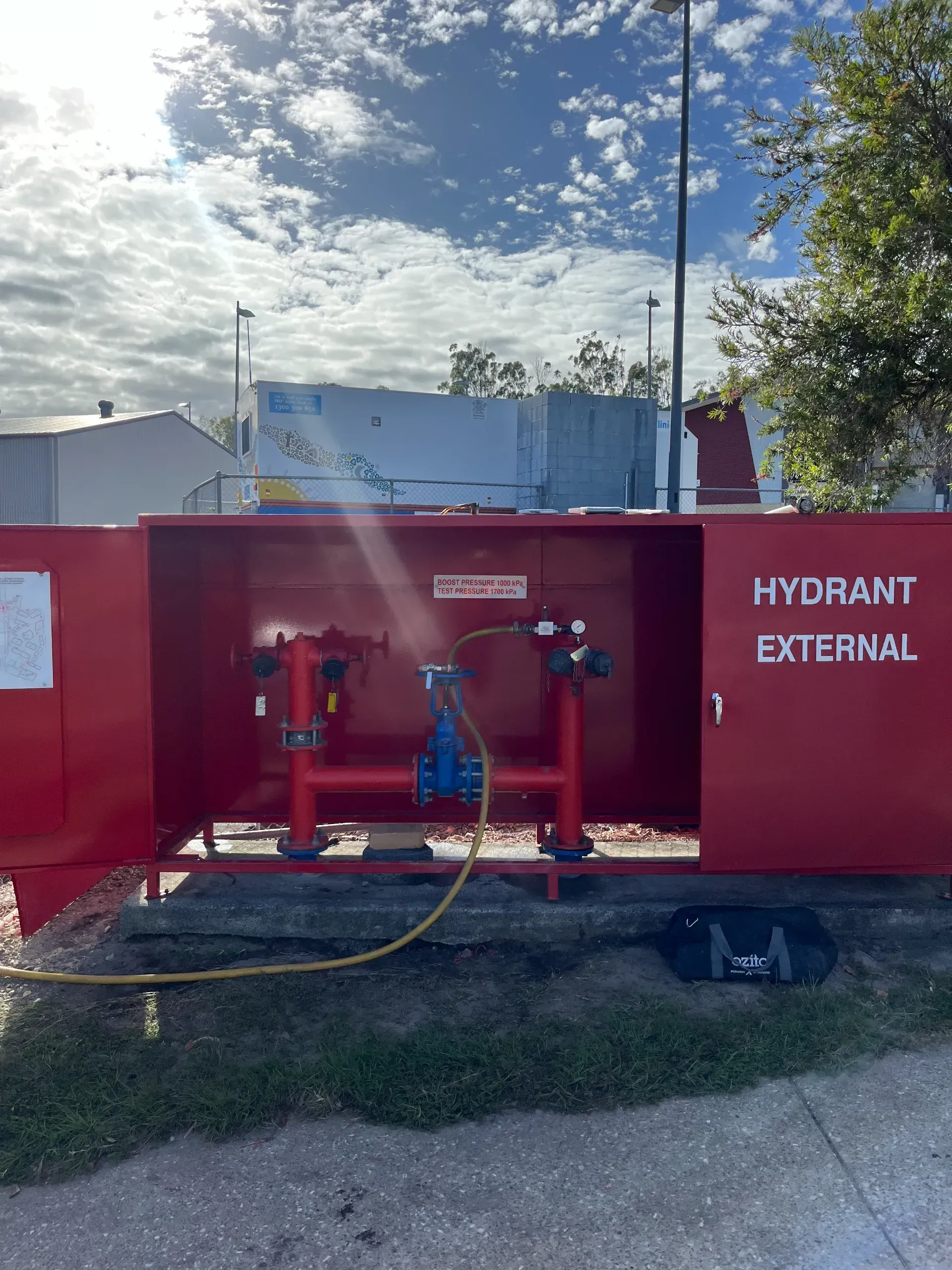 Red external fire hydrant cabinet with open doors, a hose attached, under a cloudy sky. — Commercial Leak Detection
