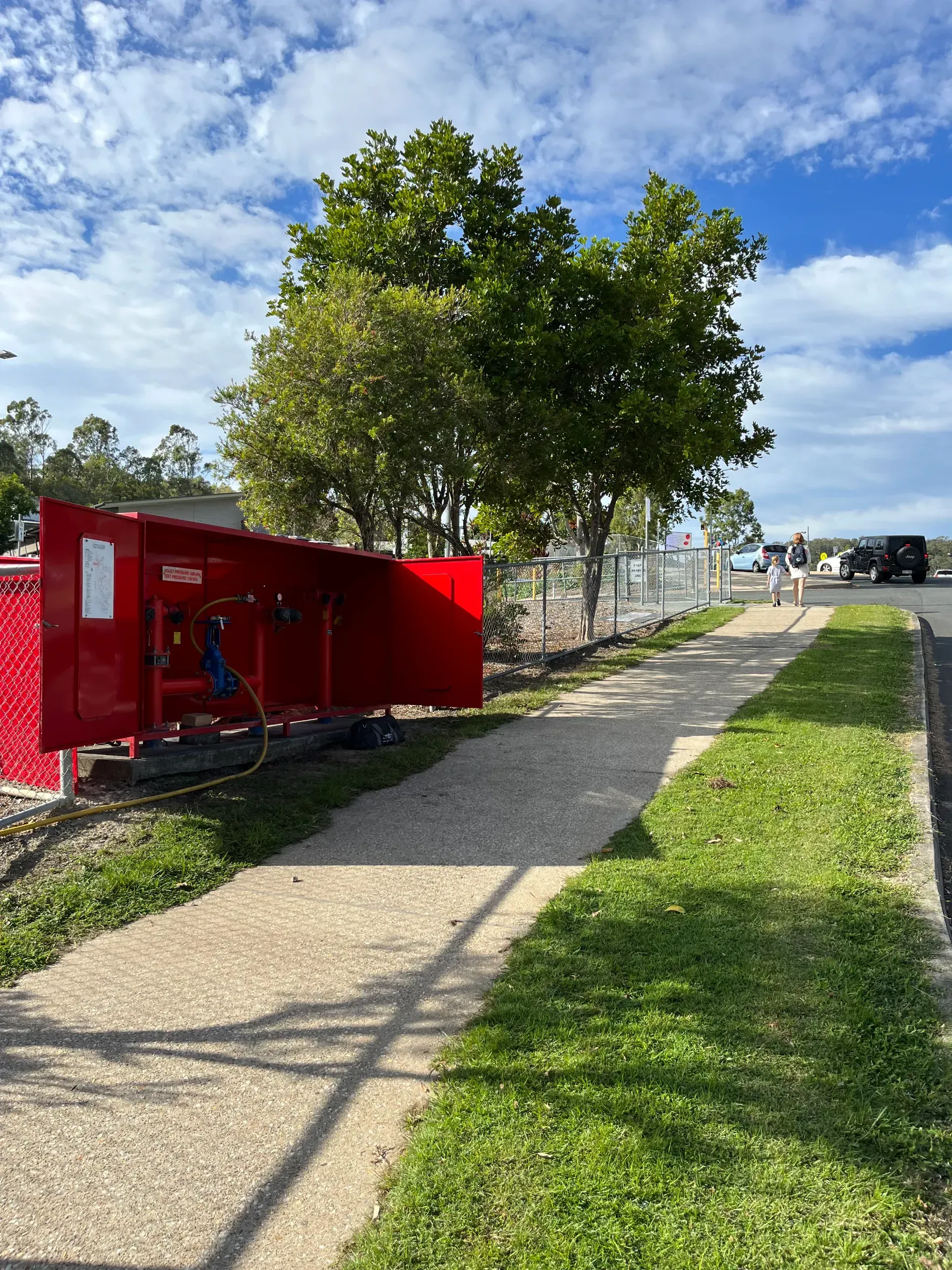 Red fire equipment box beside a sidewalk and grass, with a tree in the background. — Commercial Leak Detection