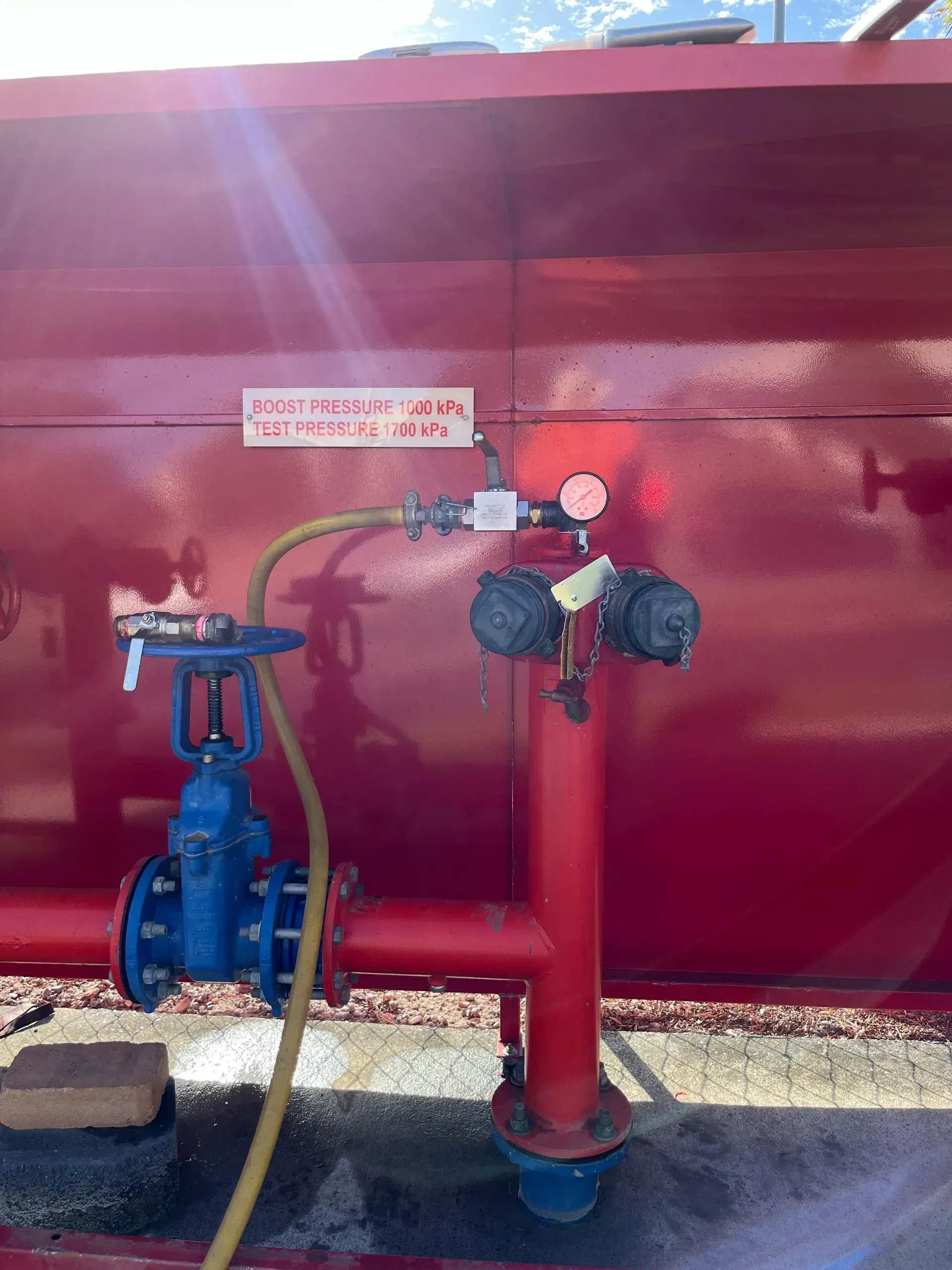 Red tank with blue valve, connected to a pipe and other fittings. Hose and gauge present. — Commercial Leak Detection