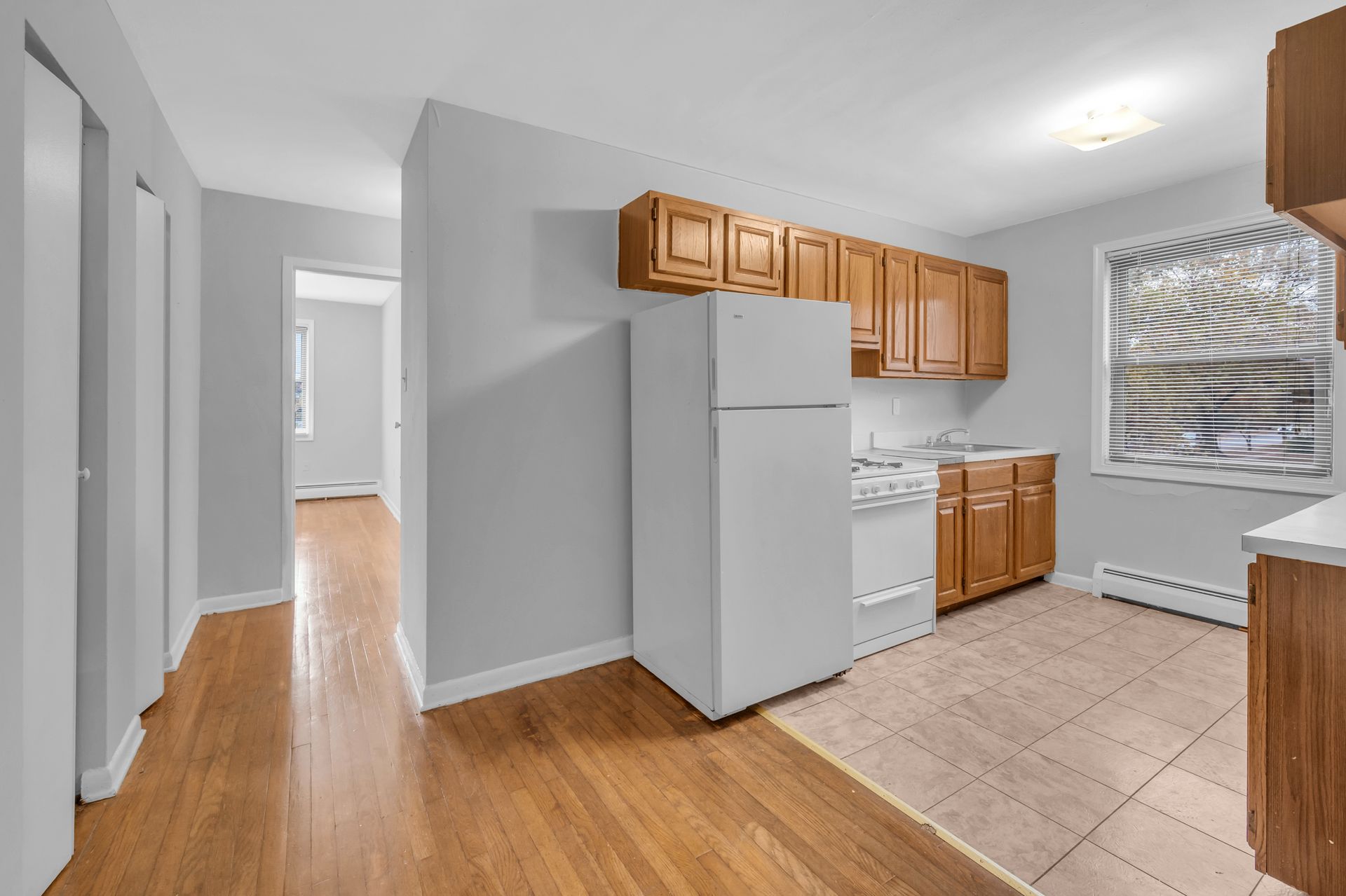An empty kitchen with wooden cabinets and a white refrigerator.