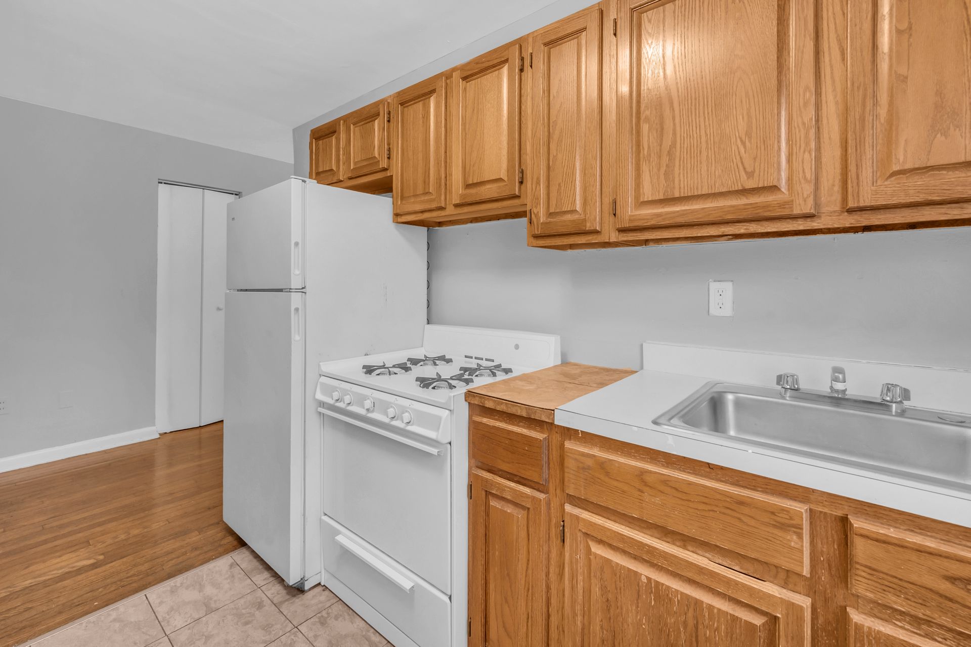A kitchen with a stove, refrigerator, sink ,and wooden cabinets.