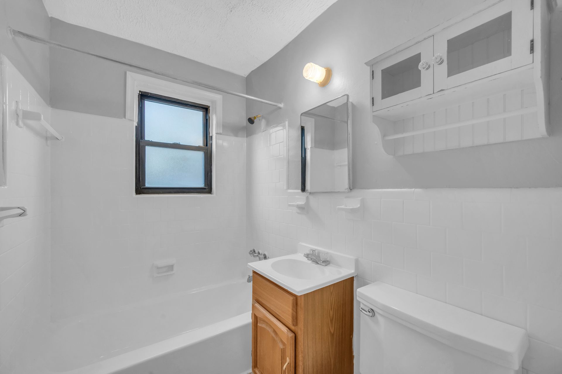 A bathroom with a sink, toilet, shower and window.