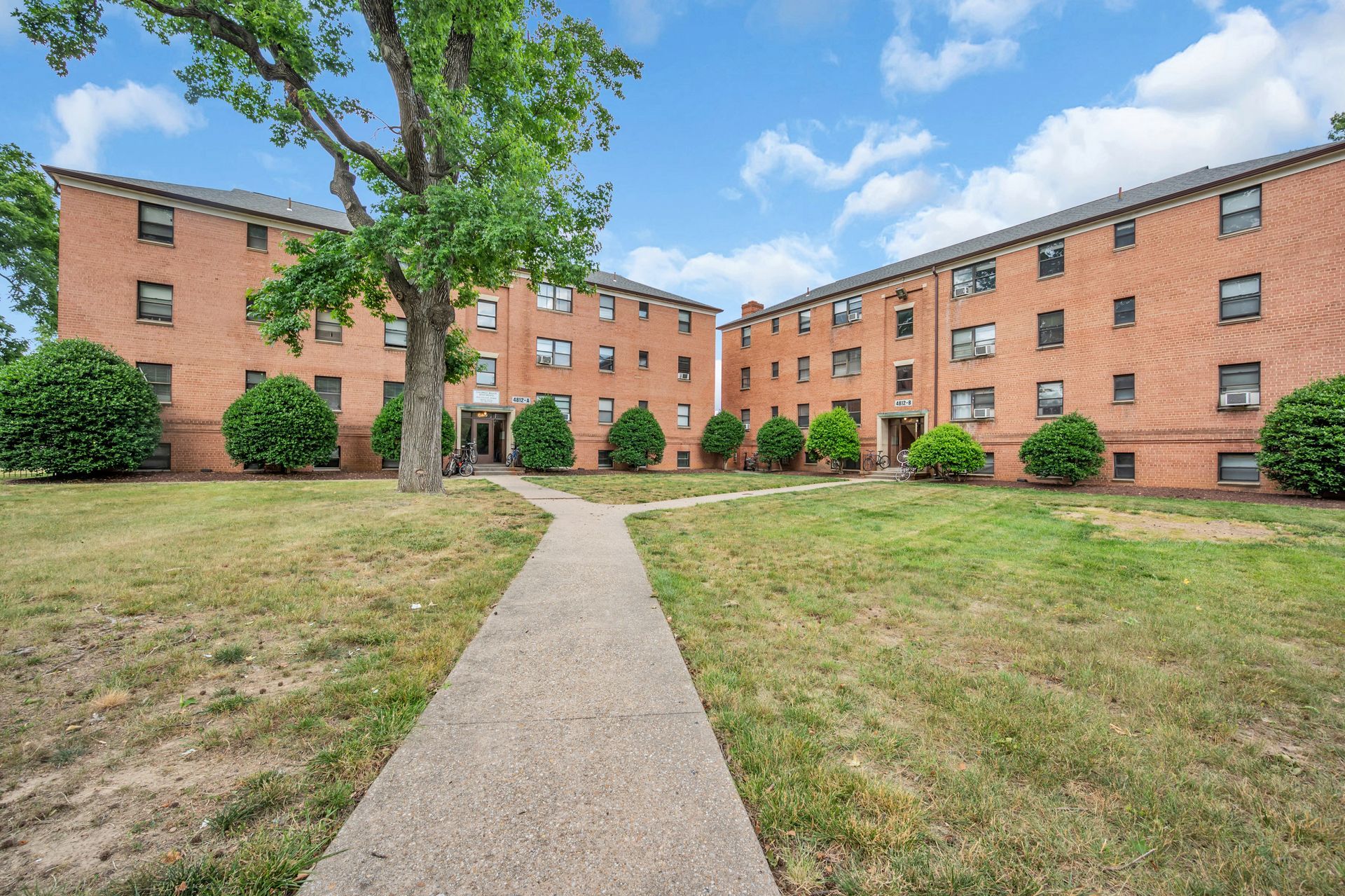 A large brick building with a tree in front of it and a path leading to it.