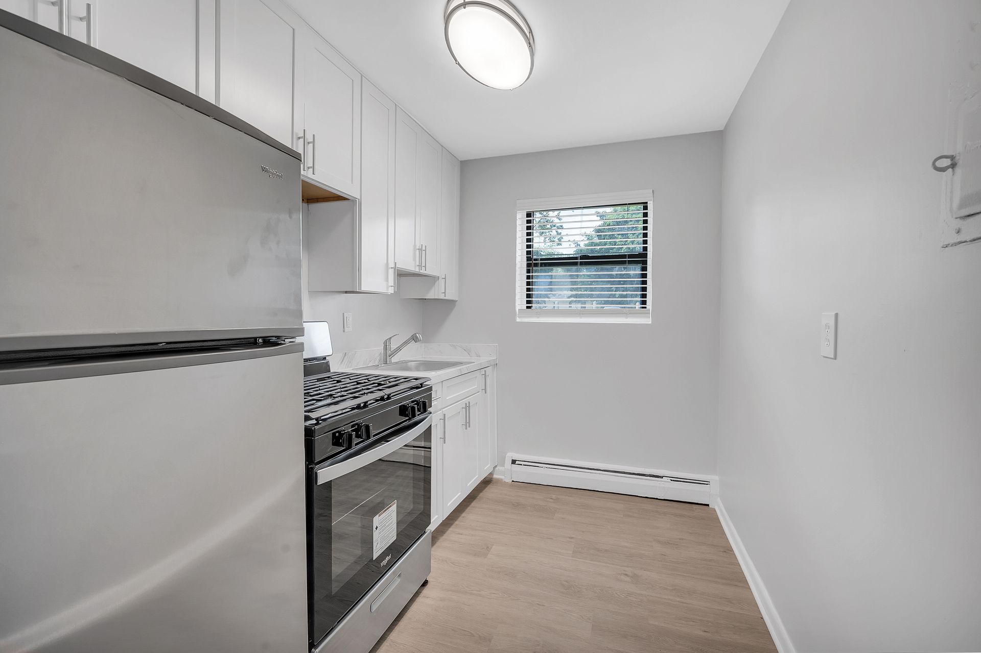 A kitchen with stainless steel appliances, white cabinets ,and a window.