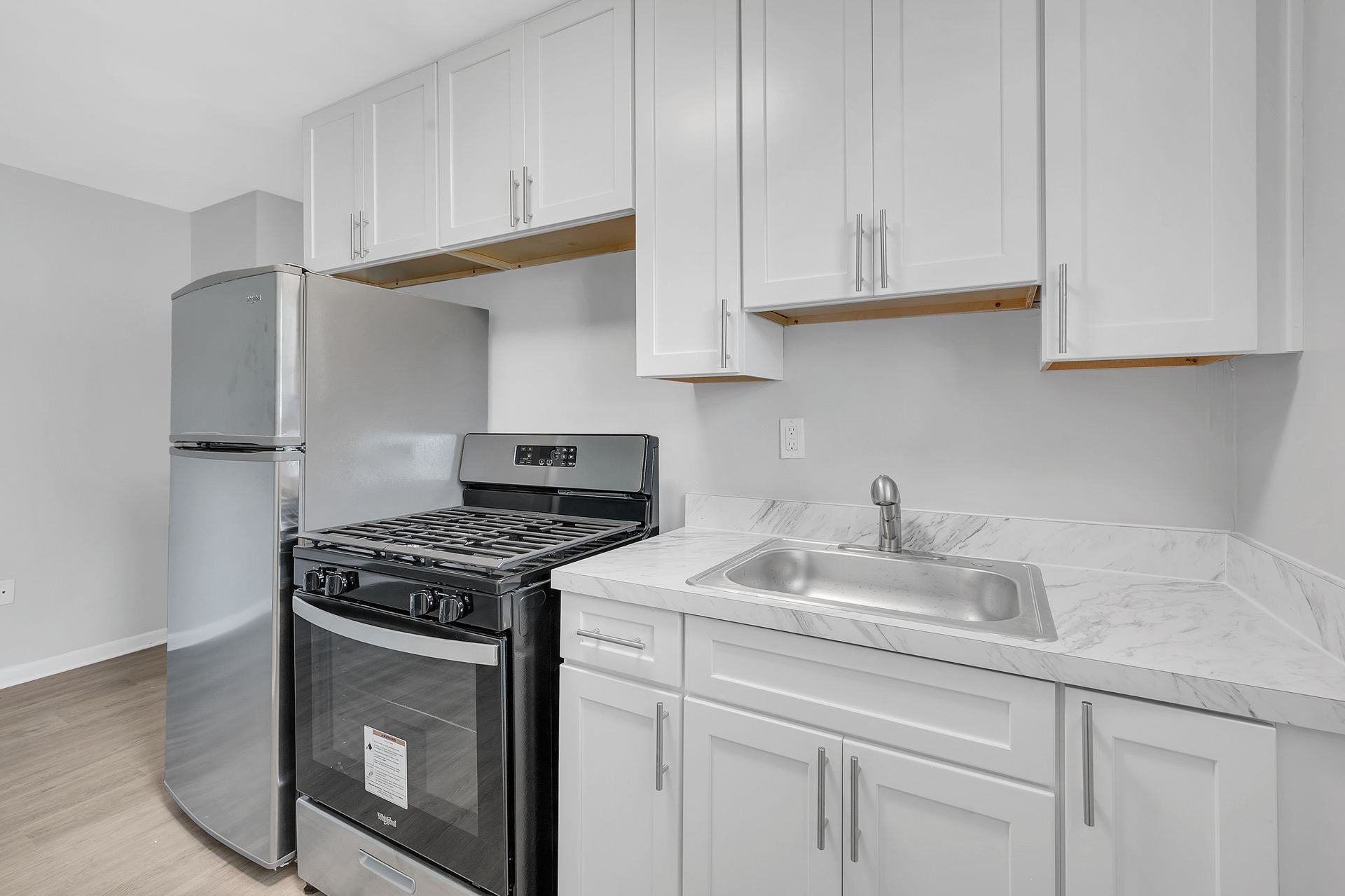 A kitchen with white cabinets, a stove, a refrigerator, and a sink.