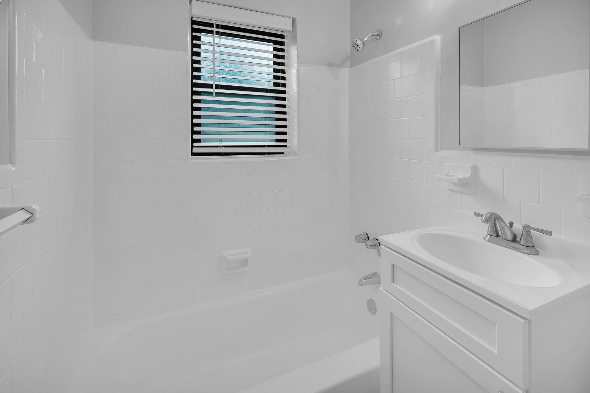 A bathroom with a sink, tub, mirror and window.