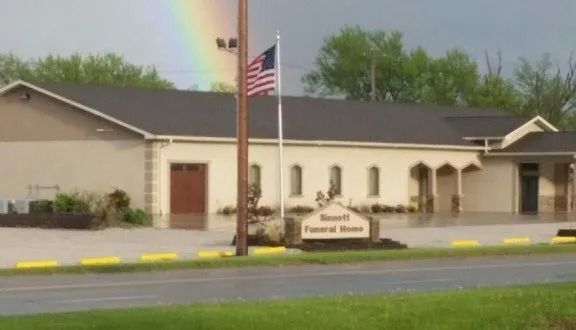 One-story cream building with American flag and rainbow over a roadside sign in front