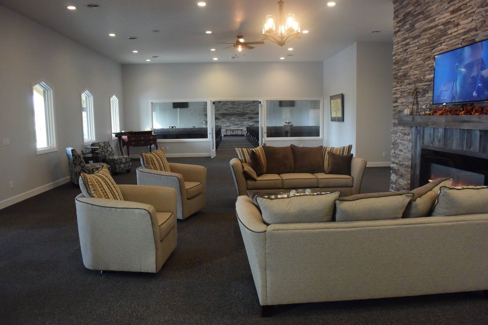 Spacious lounge with beige seating, stone fireplace, wall-mounted TV, and carpeted floor.