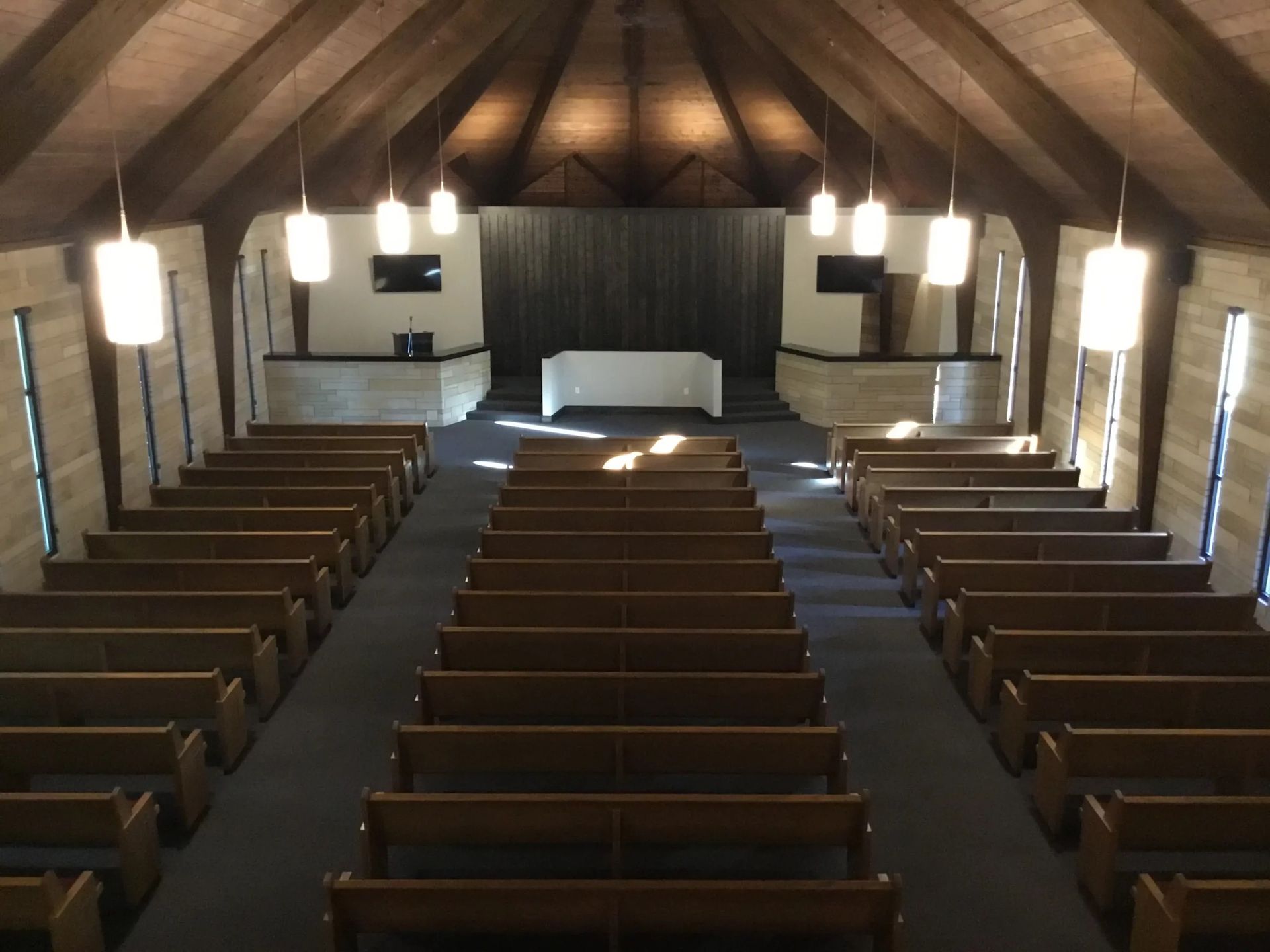 Empty church sanctuary with wooden pews, central aisle, and altar at the front under hanging lights