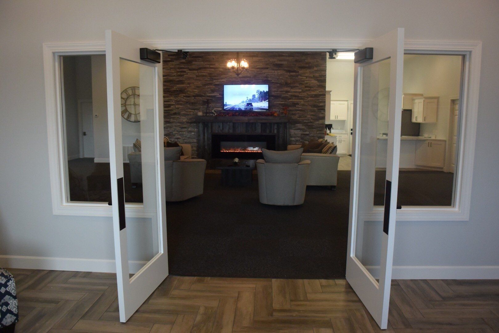 Open double doors to a cozy lounge with stone fireplace, TV, and chairs inside.