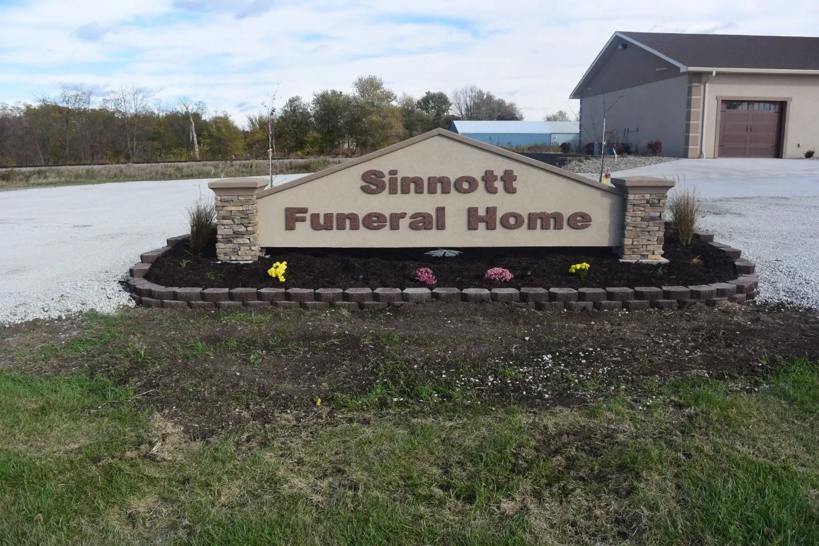 Sinnott Funeral Home sign beside a building, with flower beds and a grassy roadside