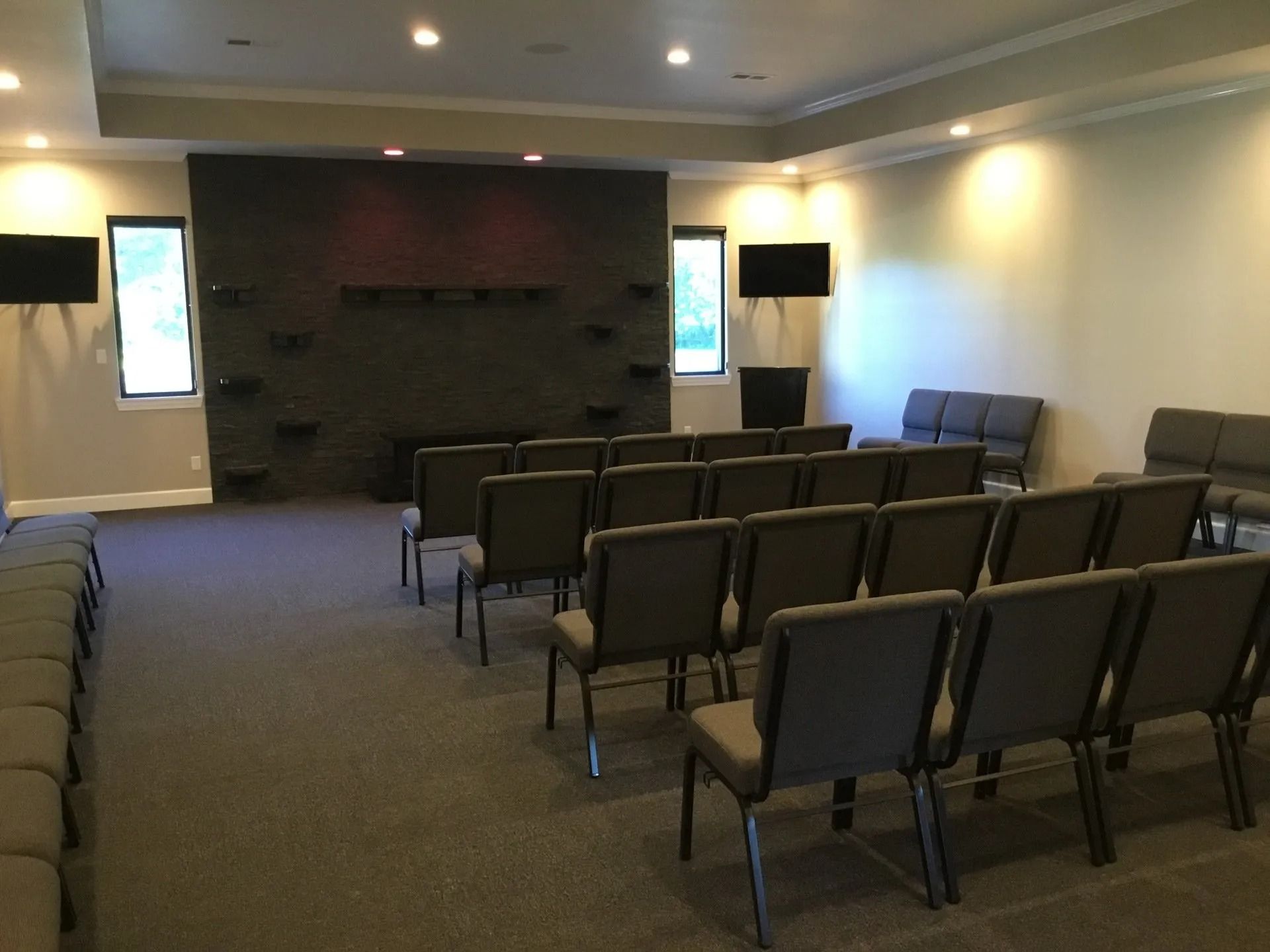 Empty conference room with rows of chairs facing a stage and large wall-mounted screens.