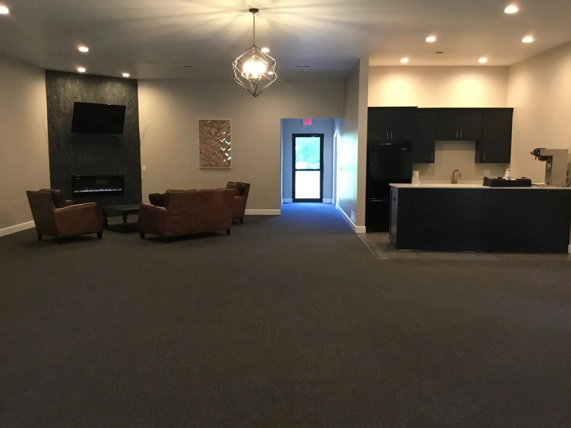 Empty hotel lobby with dark carpet, seating area, front desk, and bright doorway in the center