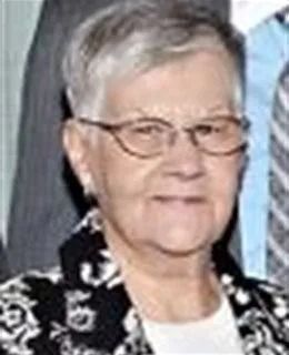 Smiling person with short gray hair and glasses, wearing a black floral jacket and white top