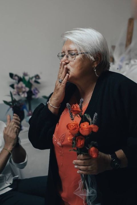 Woman in black and orange holds flowers and blows a kiss during an indoor celebration