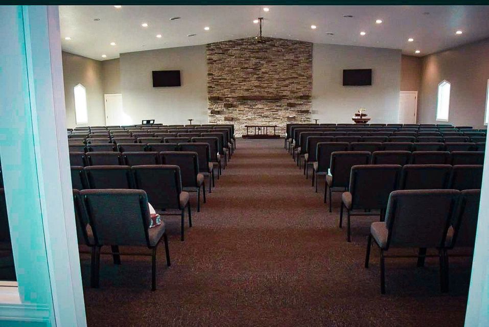 Empty church auditorium with rows of black chairs facing a stone-backed stage and altar area