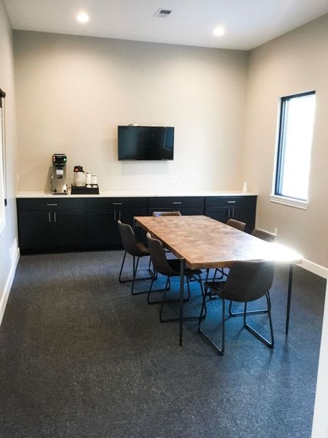 Modern meeting room with a wooden table, black chairs, wall-mounted TV, and a coffee station.