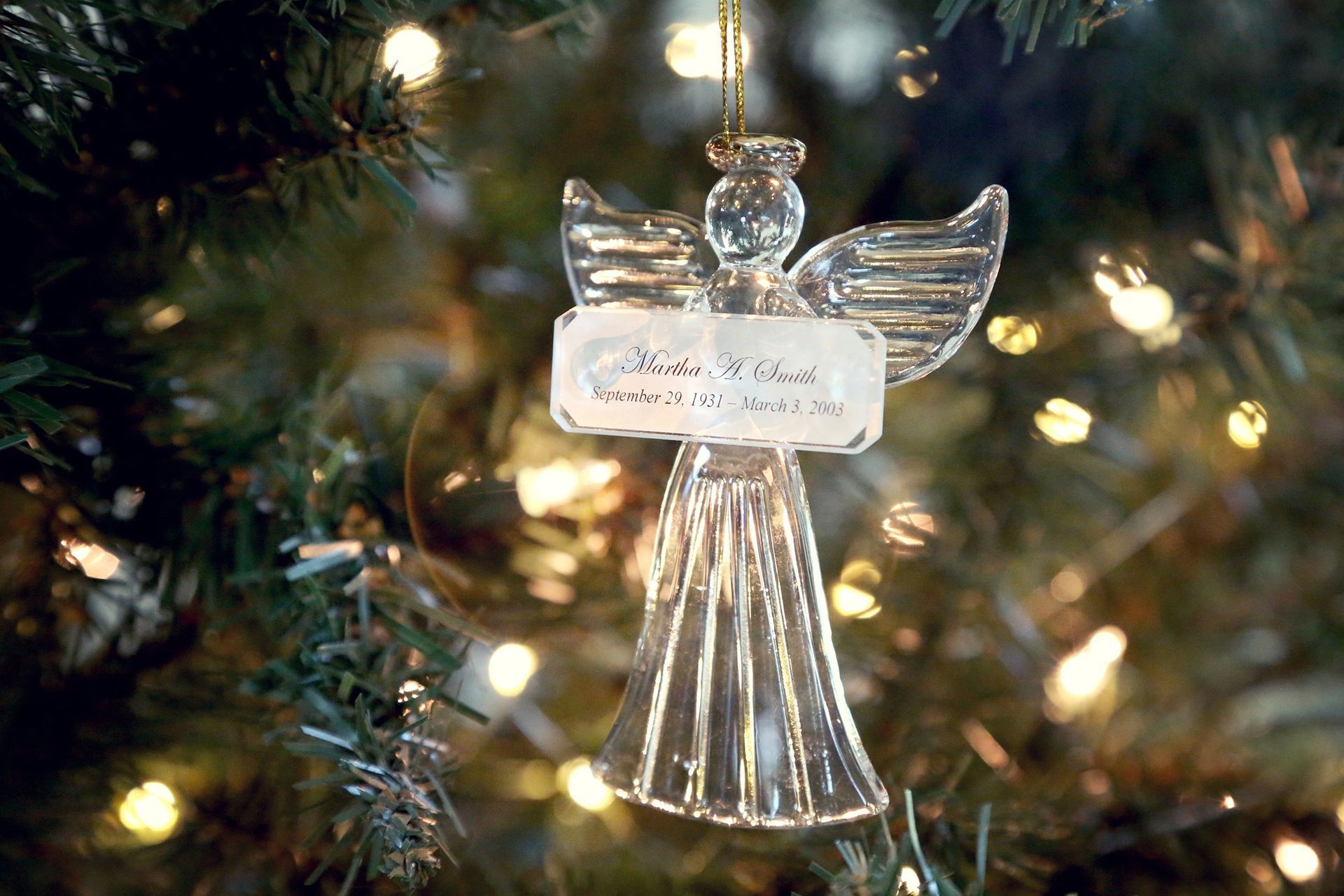 Glass angel ornament hanging on a Christmas tree with warm lights in the background