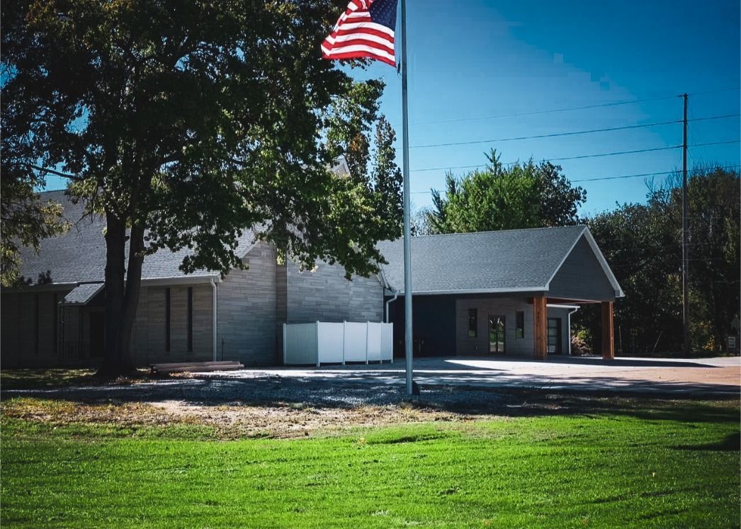 Small building with an American flag and trees beside a sunlit grassy lawn