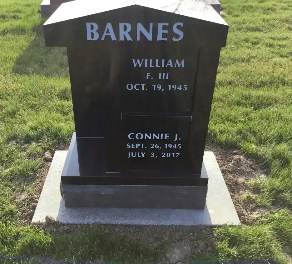 Black granite gravestone on grass with engraved names Barnes, William F. III, and Connie J.