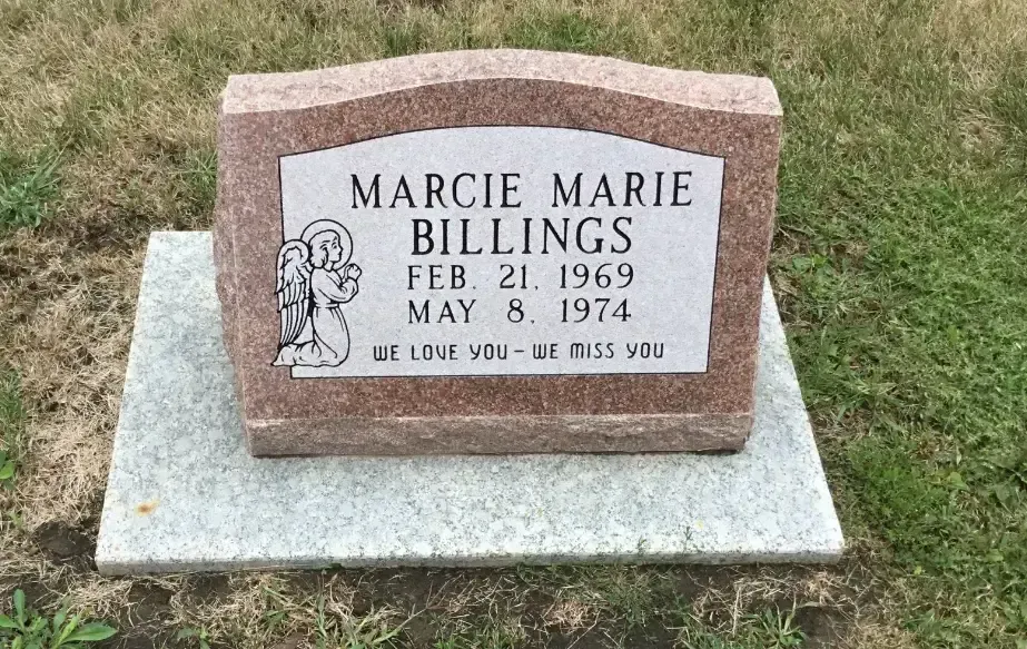 Memorial headstone with engraved plaque on a concrete base in a grassy cemetery.