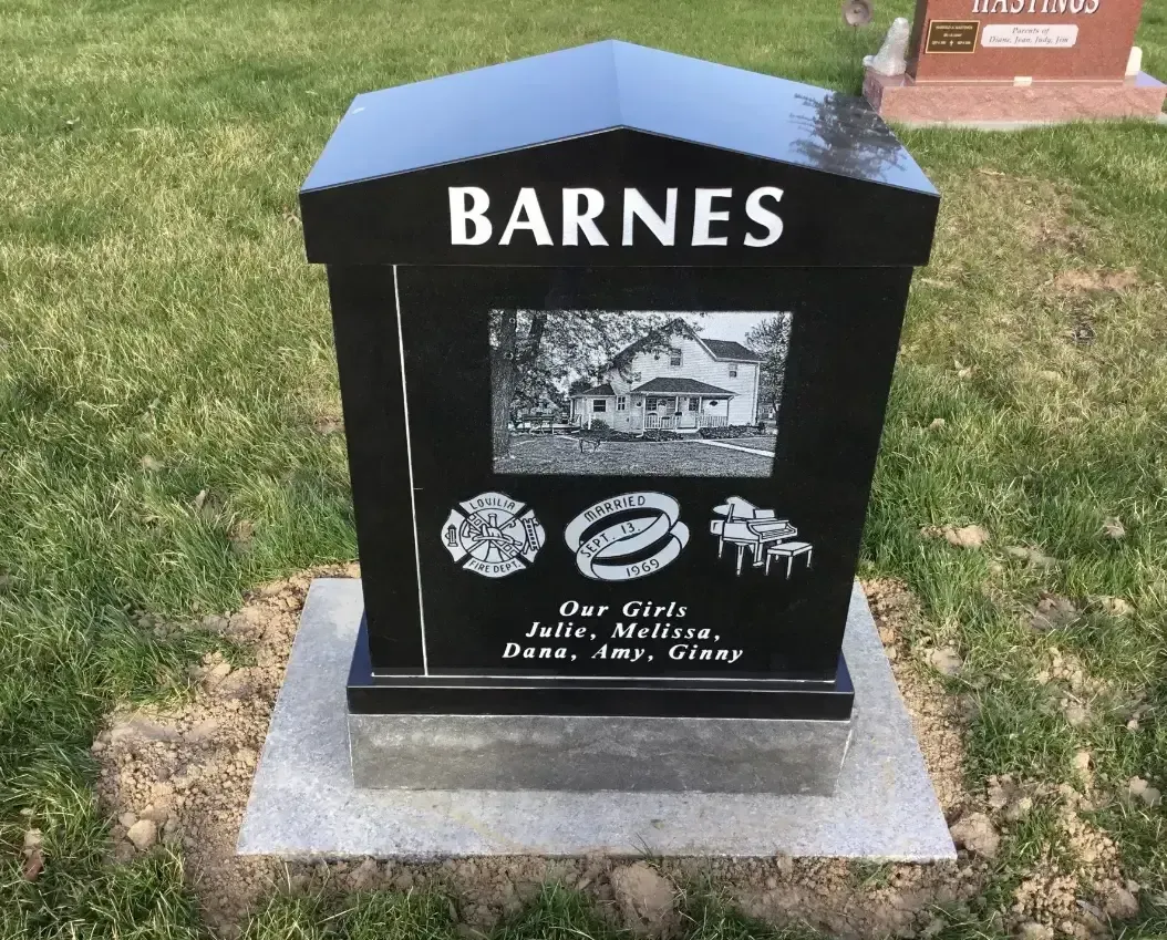 Black Barnes headstone on a concrete base in grass, with engraved photo and memorial symbols.