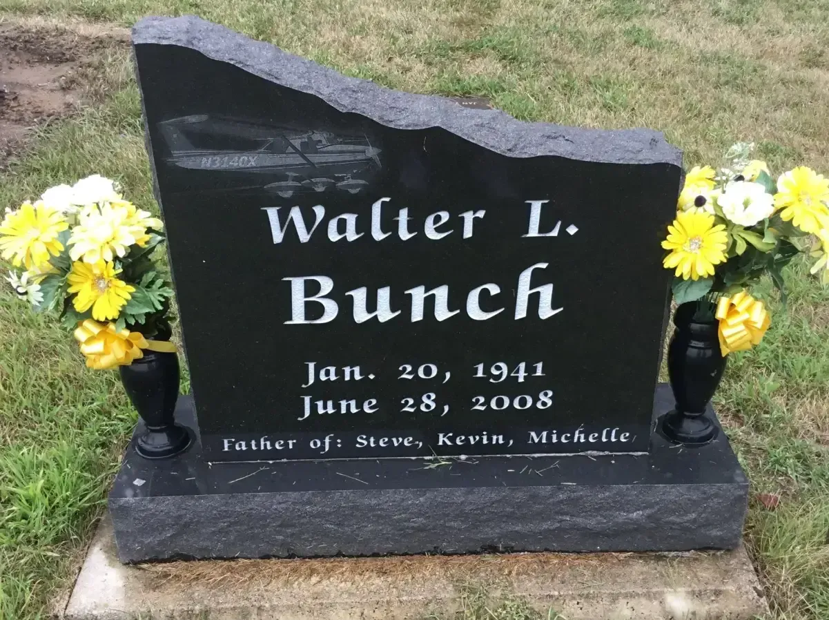 Black gravestone for Walter L. Bunck with yellow flowers on each side in a grassy cemetery