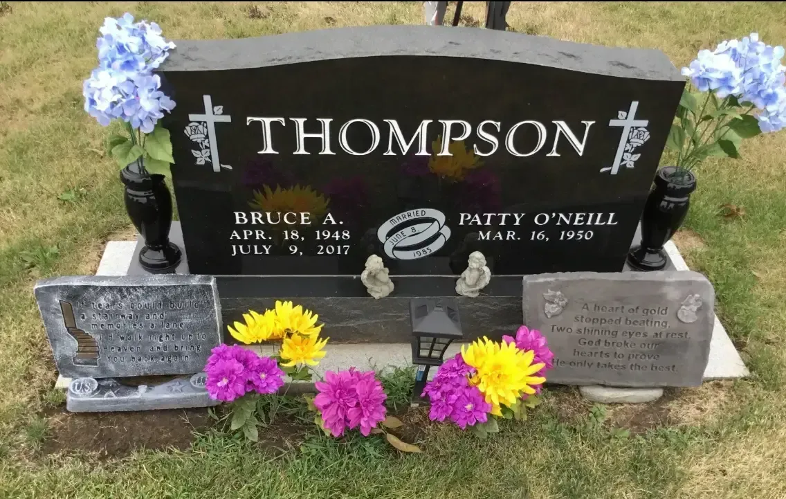 Black Thompson gravestone with blue flowers and colorful bouquets in a cemetery