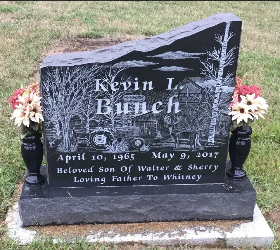 Black granite memorial headstone with floral engravings and flowers on either side for Kevin L. Bunch.
