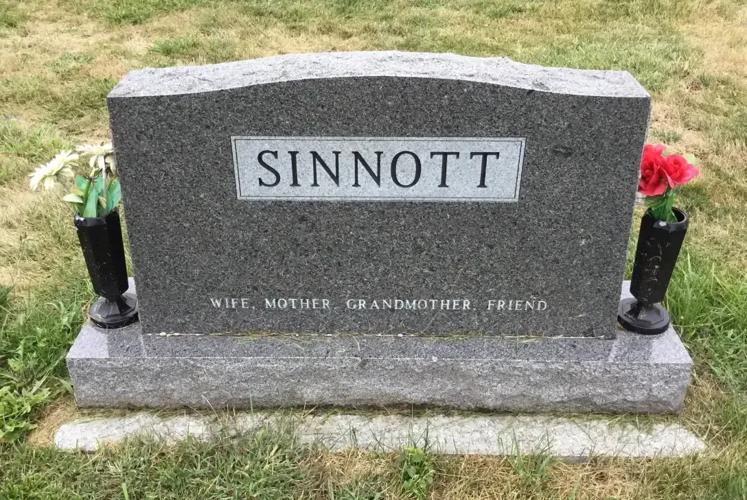 Gray granite gravestone with “SINNOTT” plaque and flower vases on a grassy lawn