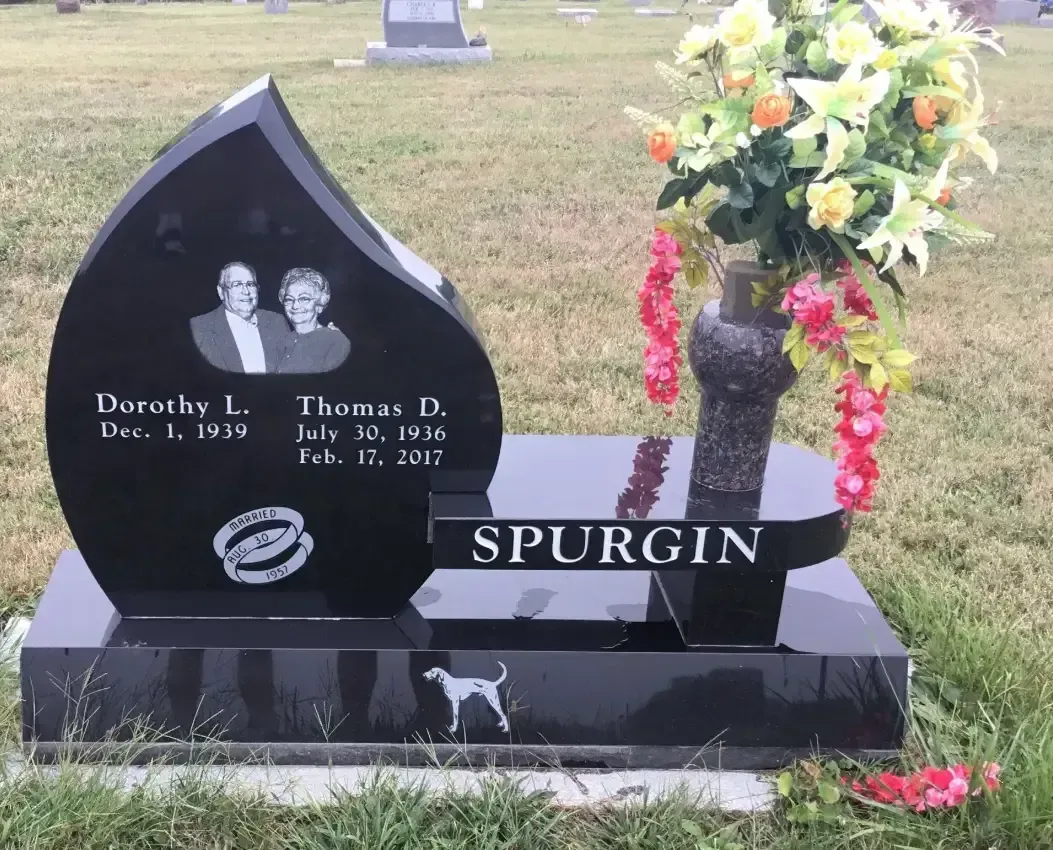 Black headstone with flower arrangement and “SPURGIN” engraving in a cemetery