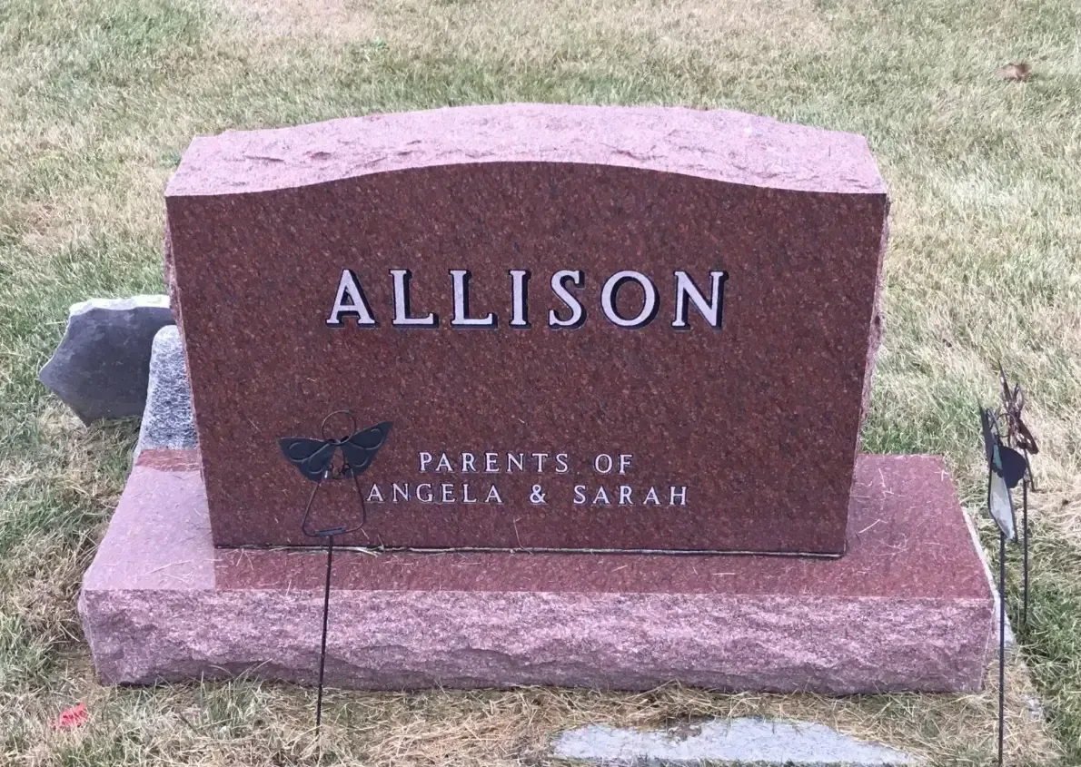 Pink granite gravestone engraved “ALLISON” in a grassy cemetery.