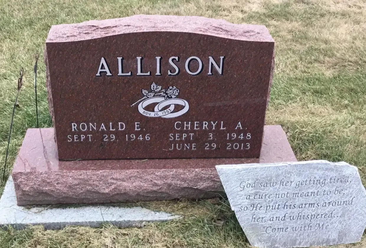 Pink granite Allison gravestone in a cemetery with a small plaque beside it.