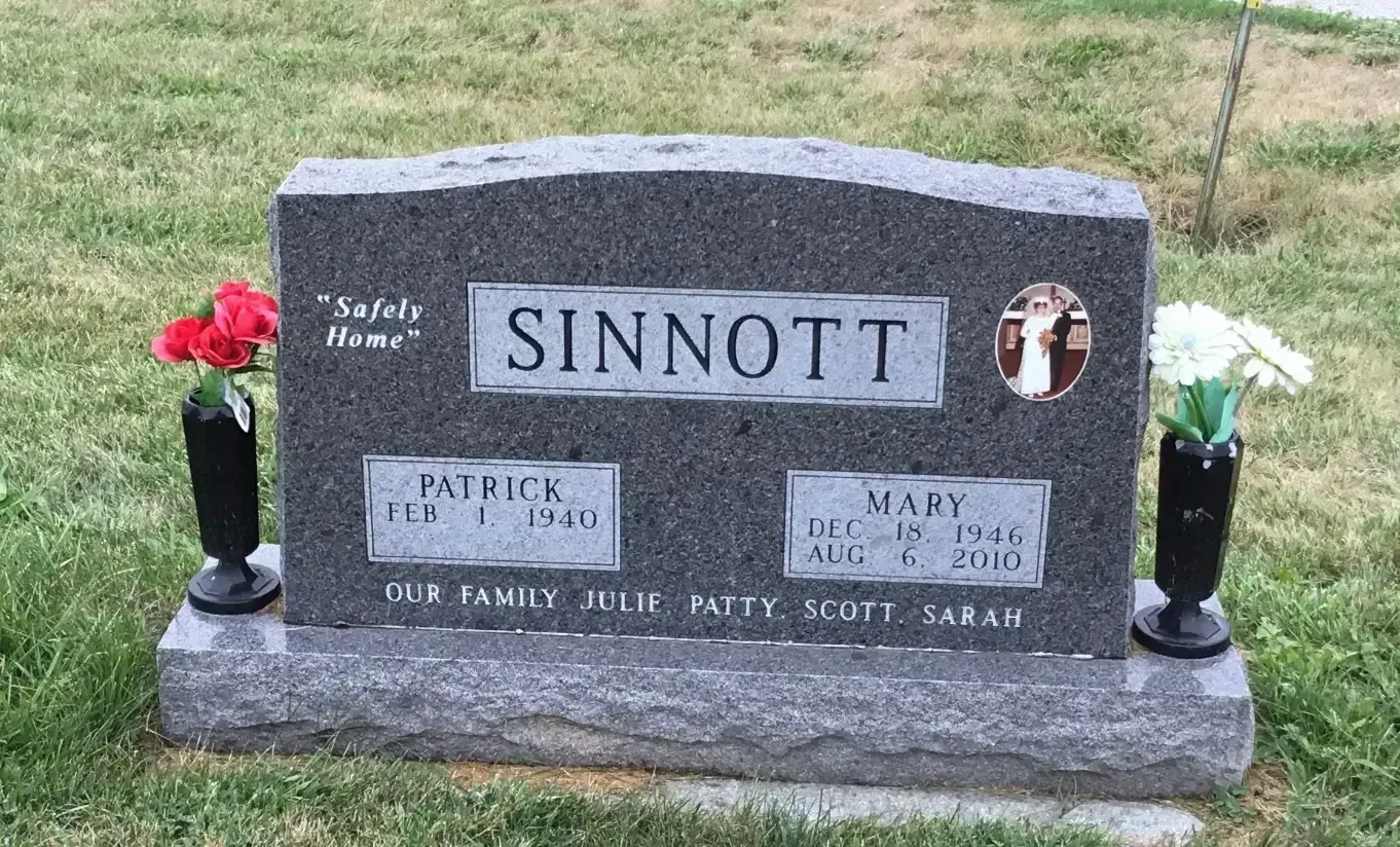 Sinnott family gravestone with engraved names and red and white flower vases on a grassy lawn