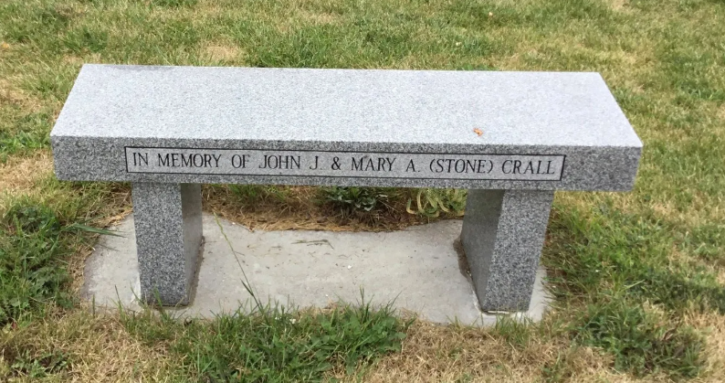 Stone memorial bench with engraved dedication in a grassy outdoor setting