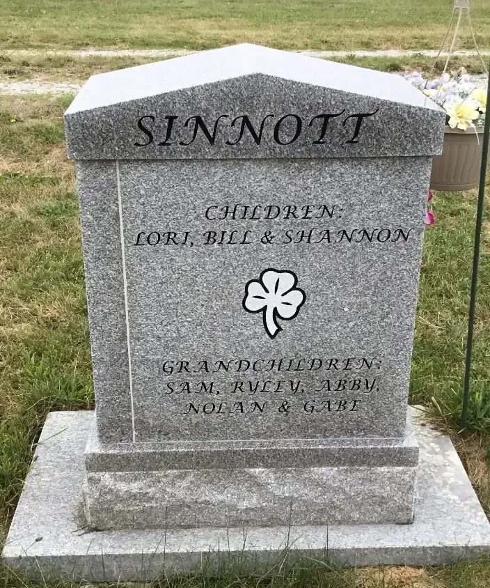 Gray granite memorial marker reading “SINNOTT” with clover symbol, in a grassy cemetery.